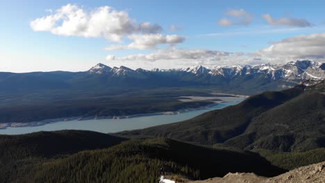 aerial panorama shot of a vast valley with green pine trees and a beautiful mountain range with rocky snowy peaks in the background on a sunny day, wide shot, conservation concept