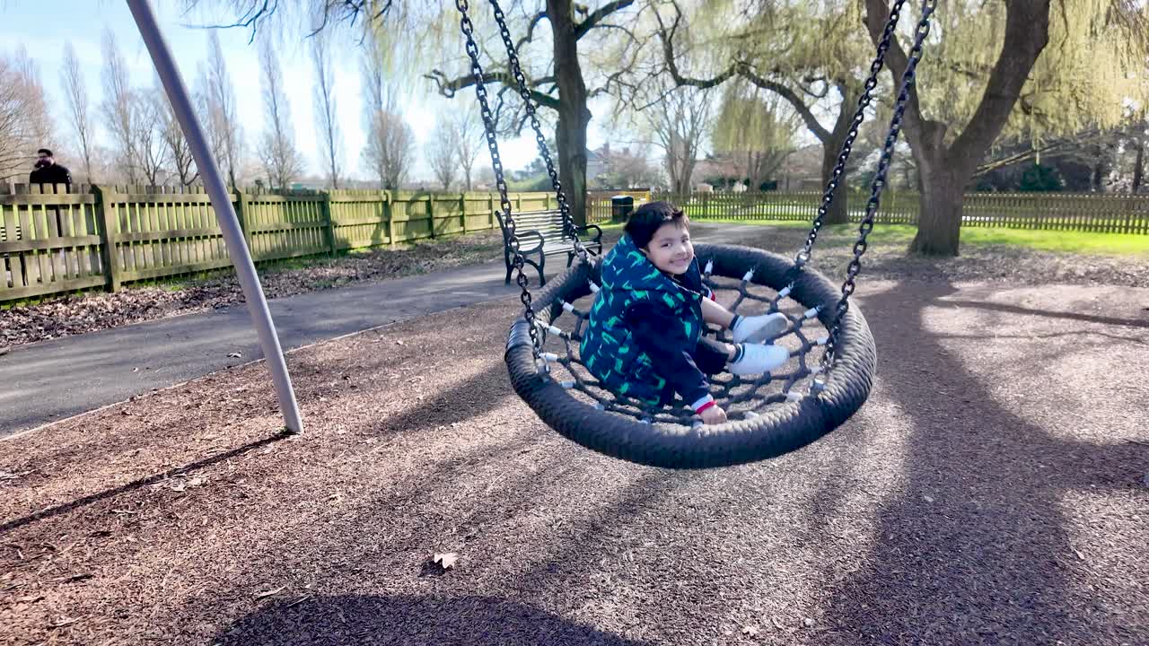 Ragazzo felice che si gode l'altalena nel parco giochi in un parco soleggiato con alberi.
