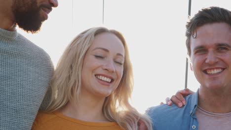 backlit portrait of smiling friends standing on bridge in city together