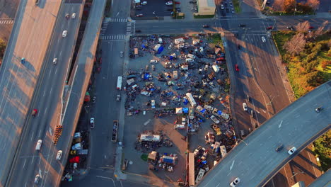 aerial overhead view of north american homeless encampment with cars driving on roads above