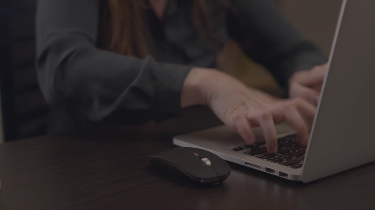 A close up of a woman's hands furiously speed typing and working on a laptop computer at a professional desk