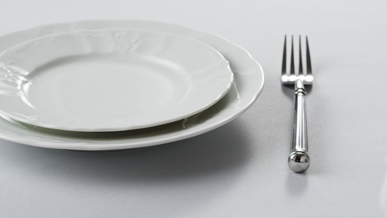 Elegant table setting with white tableware plates, cutlery, and glassware for a classy dining, fancy expensive restaurant dinner