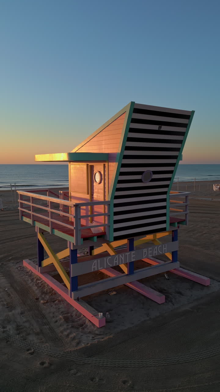 Aerial drone view of a colourful lifeguard tower on the San Juan Beach in Alicante, Spain at sunset. Vertical