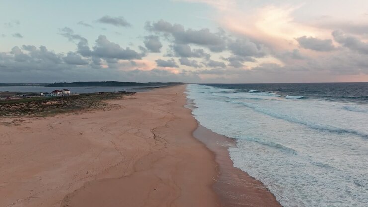 Drohnenaufnahme über einem Sandstrand mit großen Meereswellen