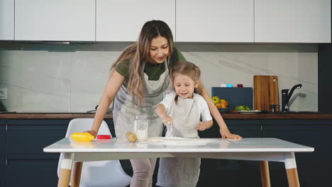 mom in kitchen hugs young daughter from behind