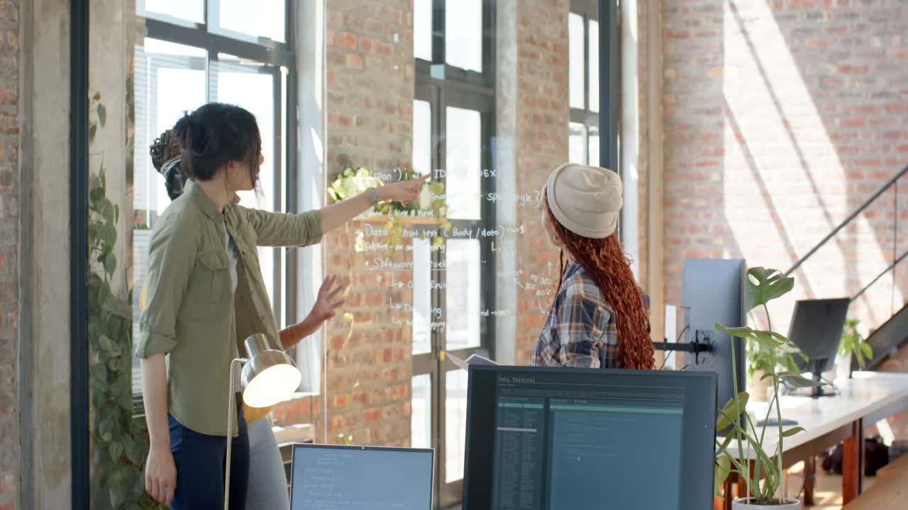 Collaborating on coding project, diverse female team discussing ideas at whiteboard in office