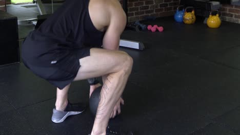 muscly man in home gym exercising throwing medicine ball on floor