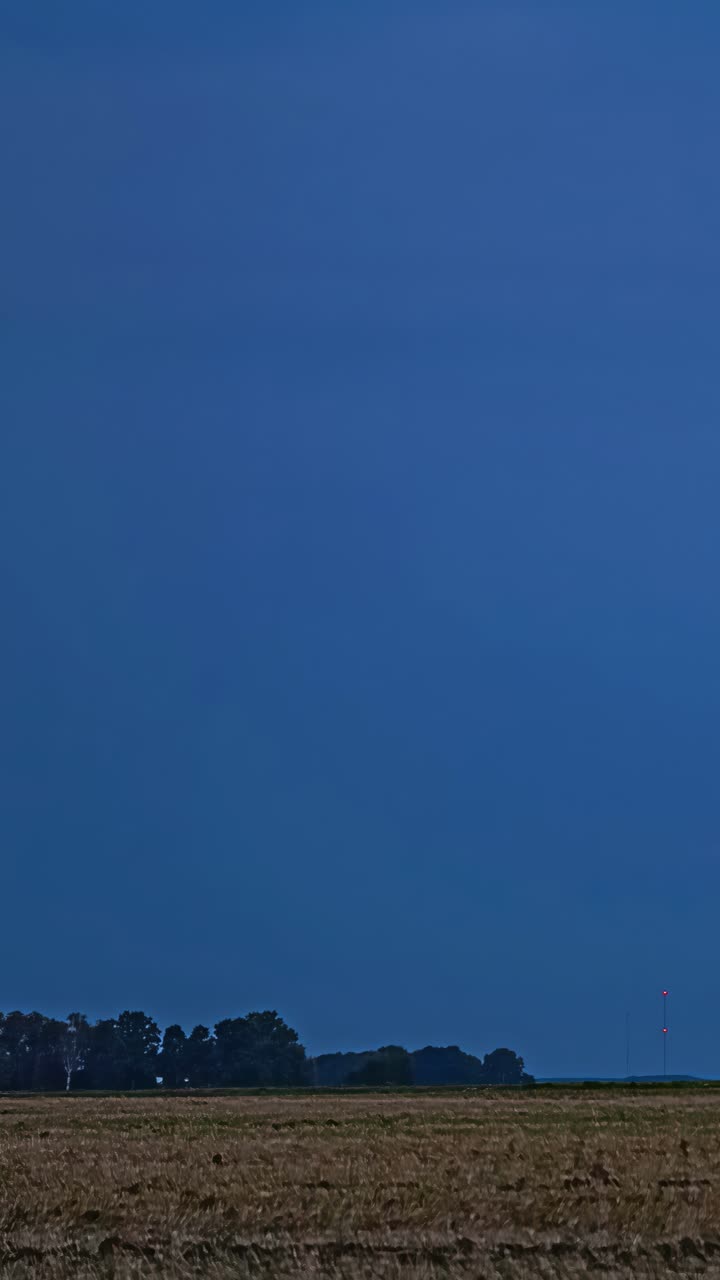 A dramatic and colorful sunset showing intense sunlight filtered through atmospheric clouds over a harvested field and distant treeline during deep twilight