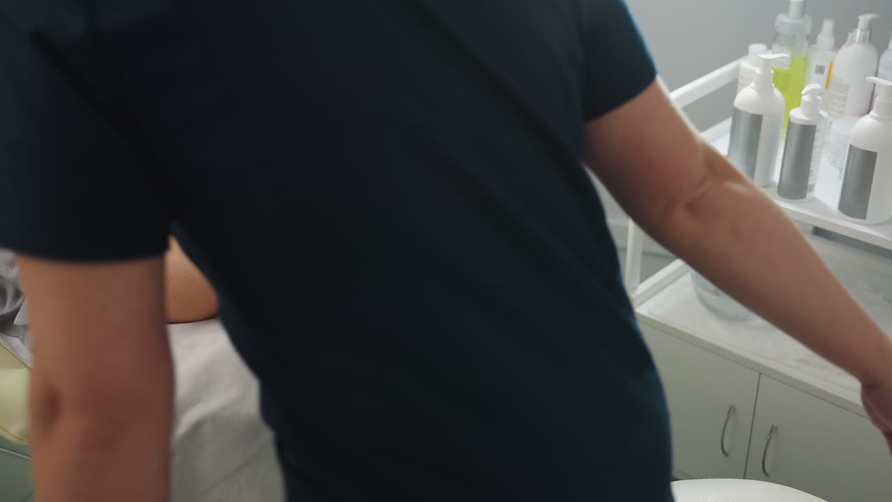High angle view of professional massage therapist walking to seat beside client head placing gentle hands on head over white linen showcasing caring service in bright therapy room environment
