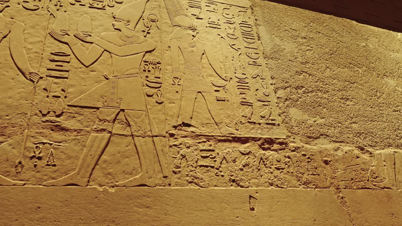 Close-up view of a large, low-relief carving on a yellowish-brown stone surface, which is likely a segment of a wall, lintel in The Grand Egyptian Museum