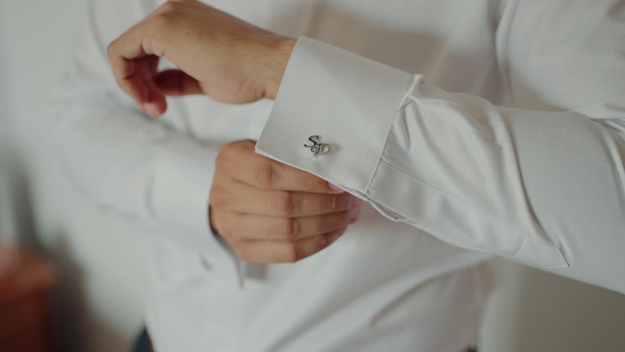 Groom fastening silver cufflinks on a crisp white dress shirt in preparation