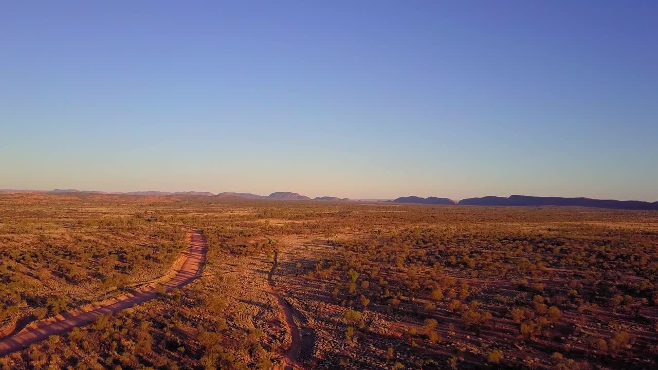 Sunset over the Central Australian Outback. Cinematic aerial track forward, following a dirt road. Filmed on a DJI Mavic Pro on a Camel Farm near Alice Springs.