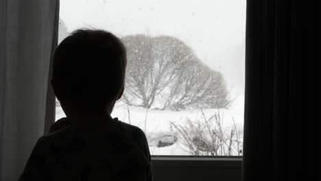 silhouette of sad young boy locked inside yearning to play outside, looking through window during covid-19 lockdown