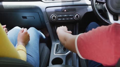 midsection of biracial sisters sitting in car and having driving lesson, in slow motion