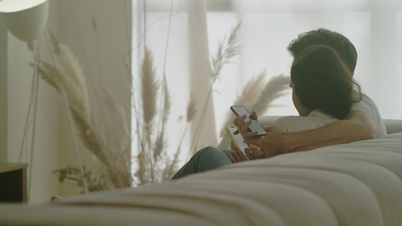 Coppia felice di spalle che guarda insieme i telefoni cellulari.