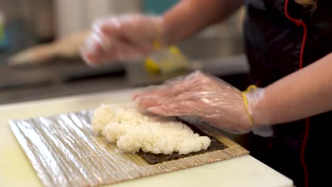 a cook places a big ball of sushi rice on nori and tries to press and form it in rectangular shape of nori