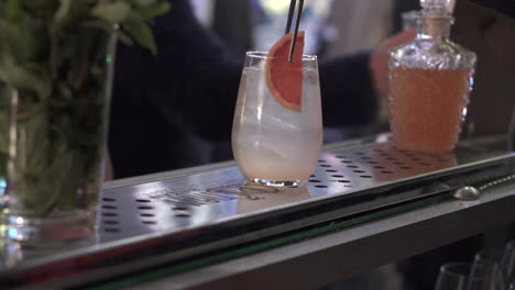 a drink being prepared on a bar, featuring a grapefruit slice, ice, and a bottle nearby