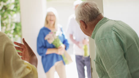 Happy-diverse-couple-greeting-group-of-senior-male-and-female-friends-at-front-door,-slow-motion