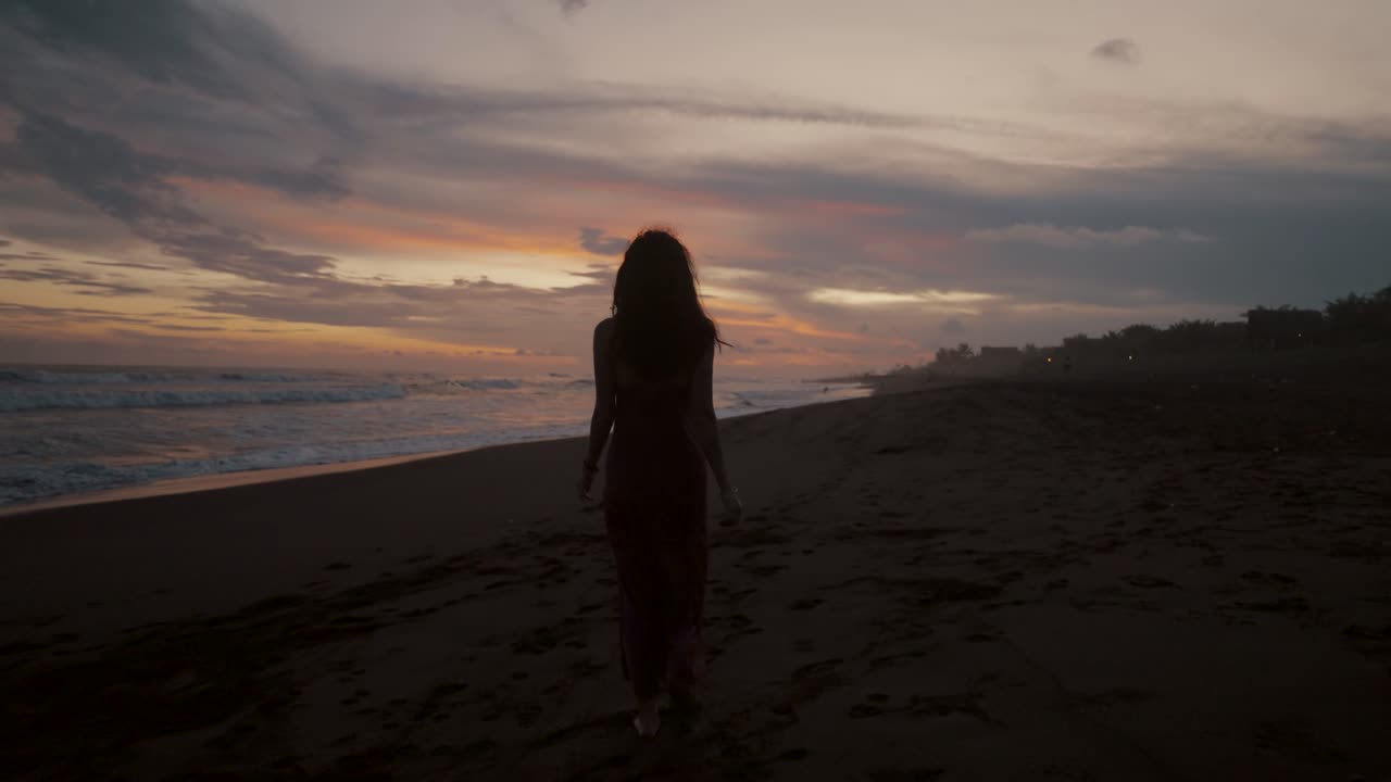 Ragazza solitaria che passeggia sulla riva di una spiaggia sabbiosa al tramonto