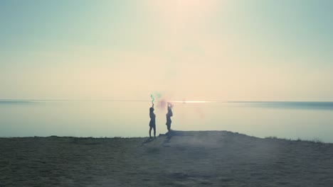 the girls with a color bombs in the hands stand on the edge of coastline