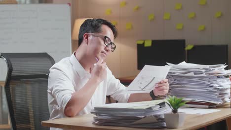 아시아인 남자가 생각하고 종이를 보고 사무실에서 문서를 처리하는 동안 지표손가락을 들어 올립니다.