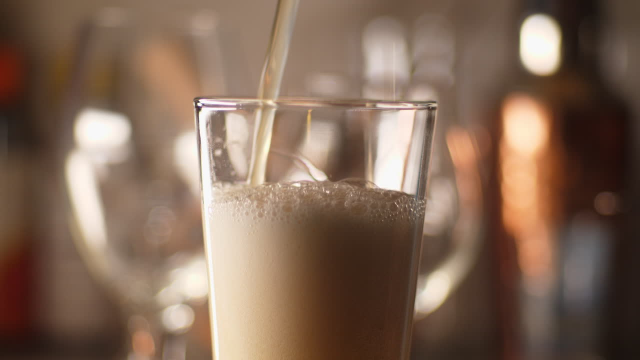 Close up of craft Beer being poured in to an empty pint glass, light background