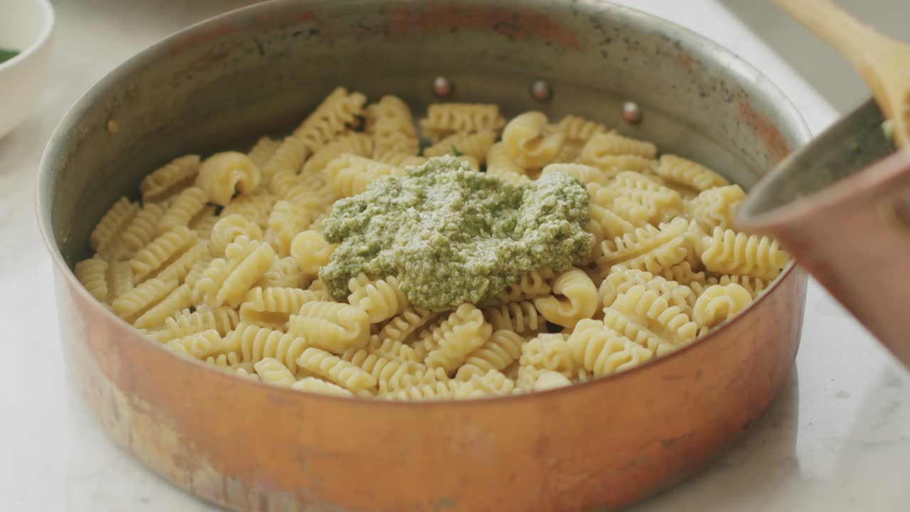 Cuoco che aggiunge il pesto nella pentola con la pasta