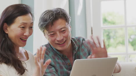 mature couple sitting on sofa at home making video call on laptop