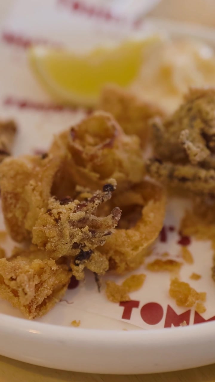 Uno scatto verticale dettagliato di calamari fritti dorati serviti con limone e salsa d'accompagnamento.