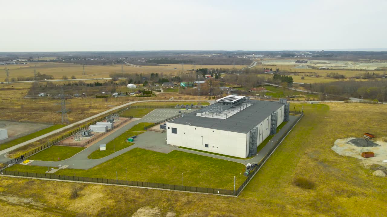 Moderne datacenterbygning og en transformerstation, der leverer strøm til anlægget, set ovenfra, mens kameraet kredser om det sikre kompleks beliggende i et landligt landskab.
