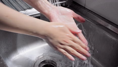 hands of woman wash their hands in a sink with soap to wash the skin and water flows through the hands