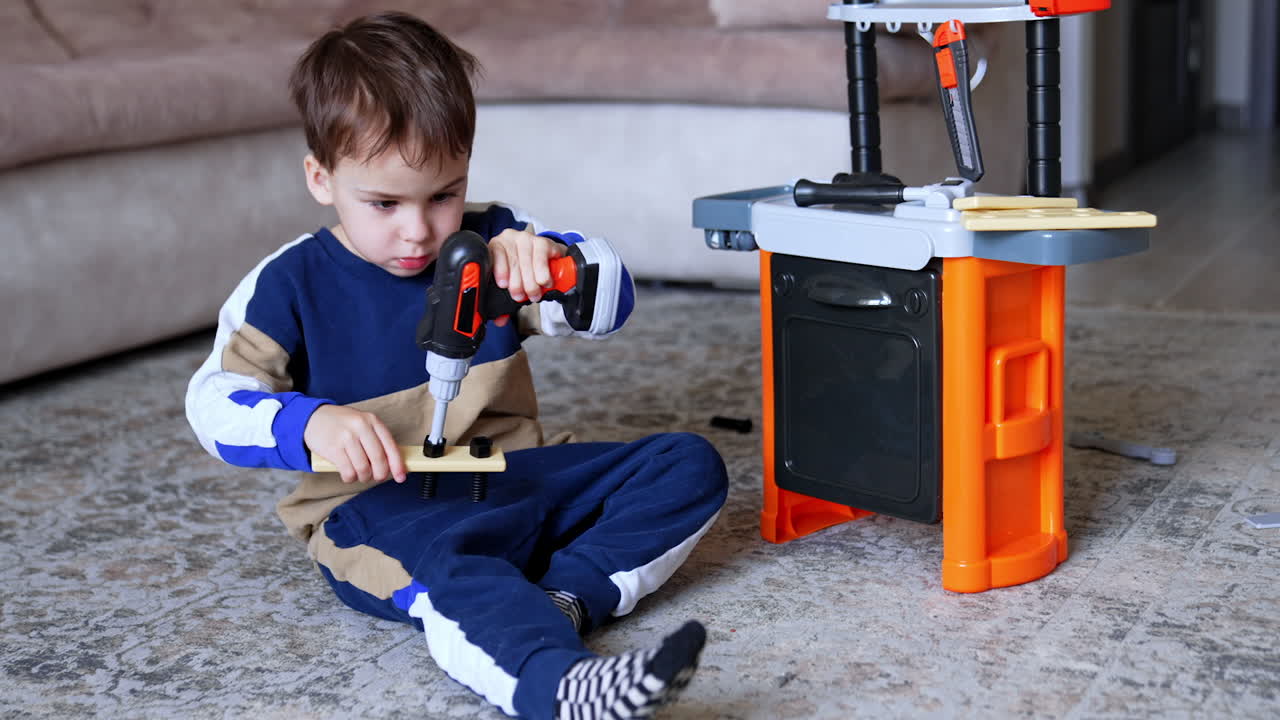 Child plays with toy tools inside. A boy plays on the floor with a toy workbench, using a toy drill to assemble wooden pieces