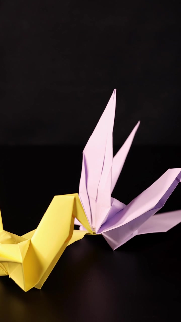 Gul origamifugl taber et blåt papiræg, studiebelysning, sort baggrund, jævn kamerabevægelse