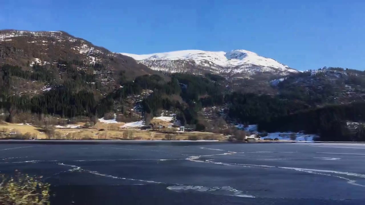Autobus viaggia lungo un lago ghiacciato e montagne innevate in una giornata limpida nella Norvegia rurale
