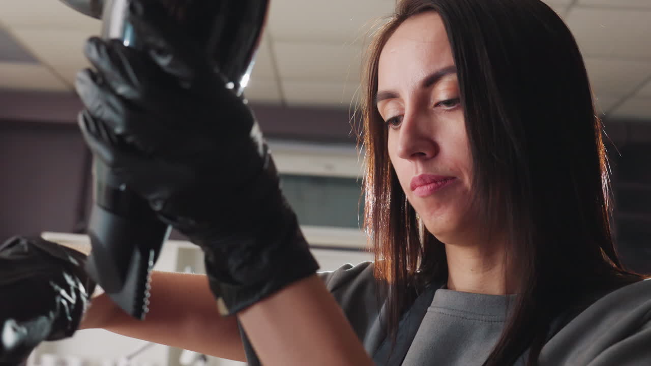 Una peluquera profesional inspecciona las herramientas de estilismo; una experta en belleza revisa el secador de pelo y el cable antes de una cita; una cosmetóloga examina cuidadosamente el secador de pelo y el cable antes de un procedimiento de estilismo.