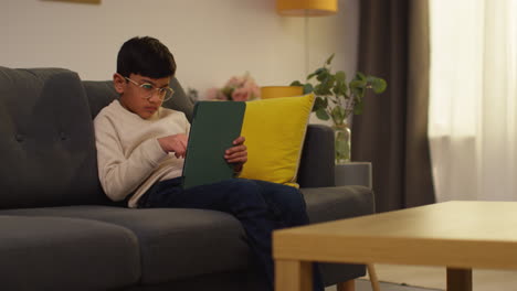 young boy sitting on sofa at home playing games or streaming onto digital tablet 8