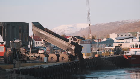 dump truck dumping load of dirt into fjord in akureyri iceland