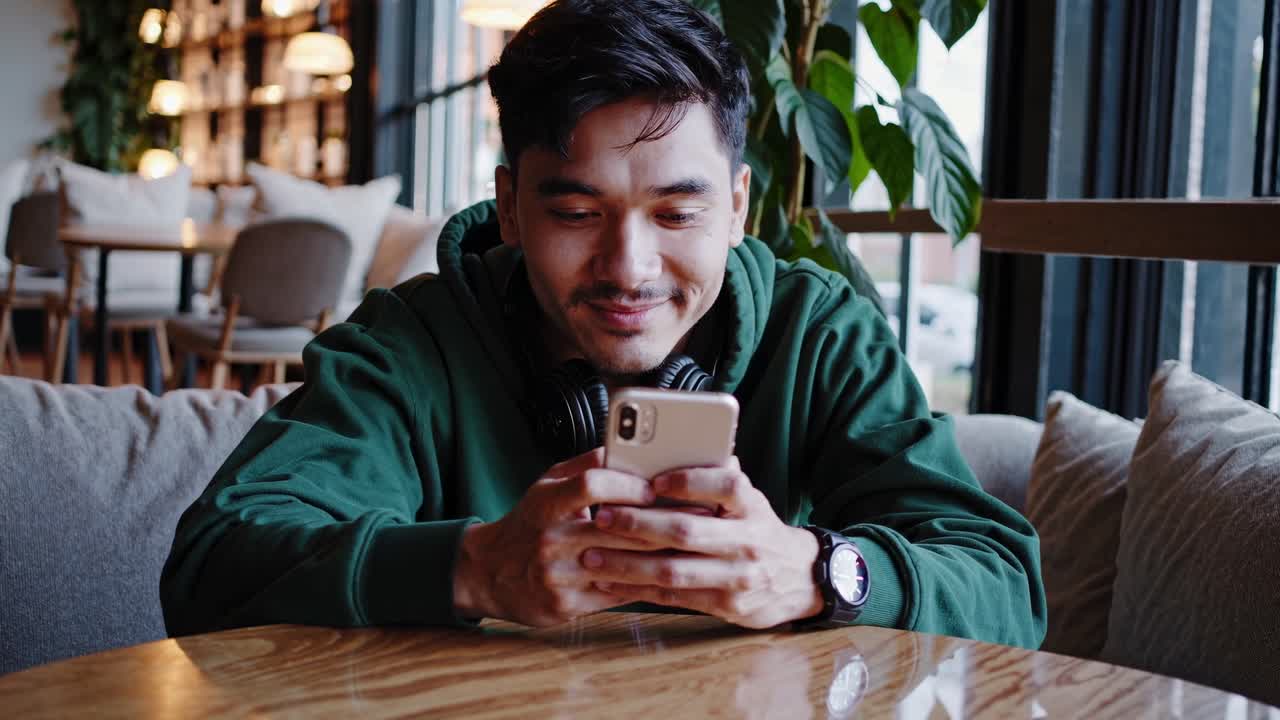 밀레니얼 세대는 현대적인 커피에서 휴식을 취하고, 창문 근처의 쾌적한 테이블에서 자유 시간을 즐기면서 진정한 미소로 스마트폰을 사용합니다.