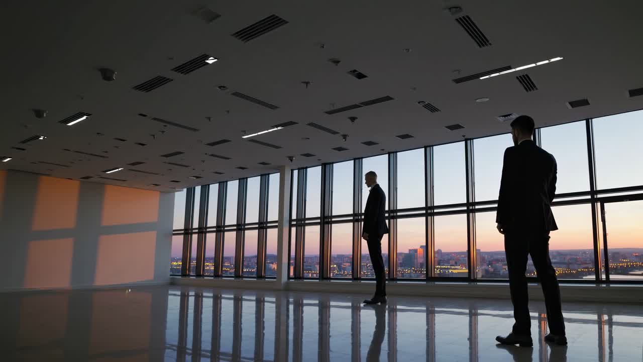 Businessmen overlooking city sunset from empty office space