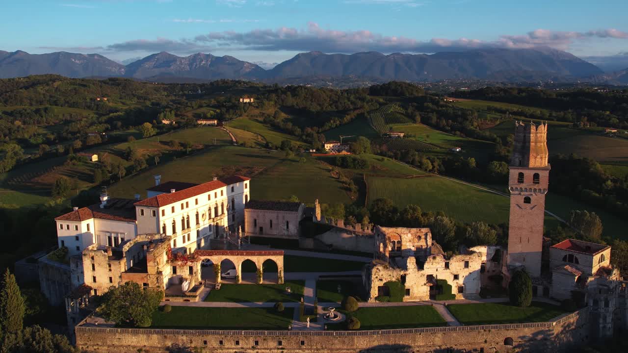 vista aérea de un castillo medieval en la cima de una colina, rodeado de viñedos de prosecco, en italia, con montañas en el fondo