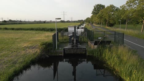 aerial shot of a small water gate installation in the dutch countryside, reflecting in calm waters.
