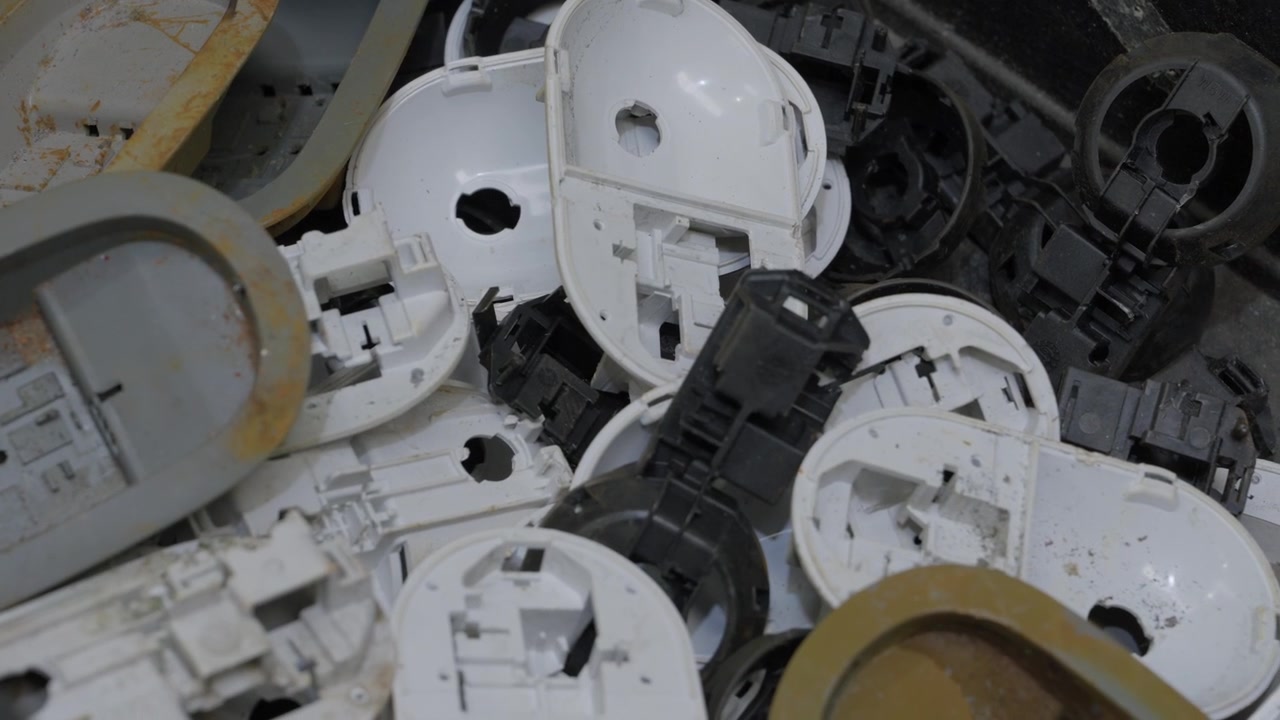 Overhead close up of mixed white grey and beige discarded plastic appliance housing components for recycling