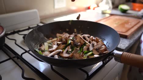 sliced mushrooms falling into the pan with green squash and parsley cooking in the kitchen