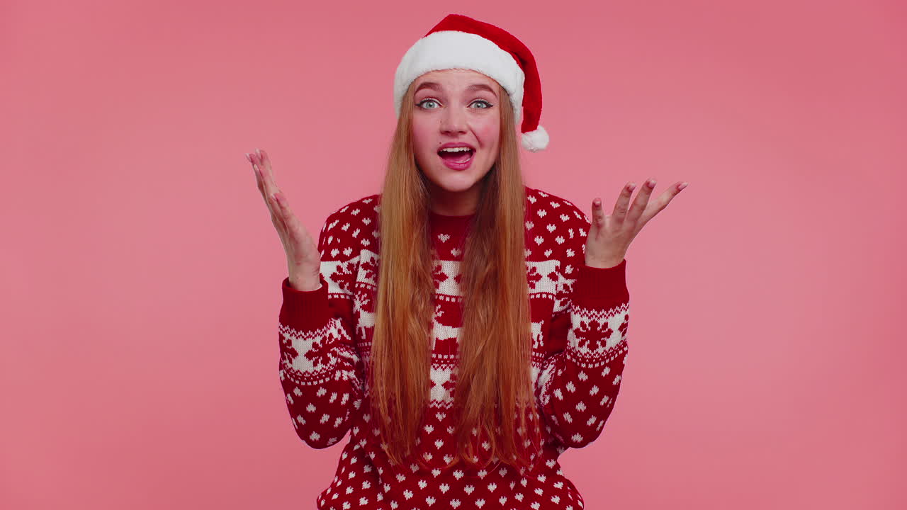 Teen adult girl in Christmas hat raising hands in surprise shocked by sudden victory, wow emotion