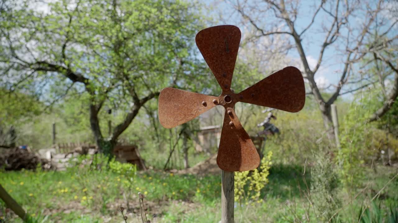 Rusty windmill in a rural garden with blooming trees