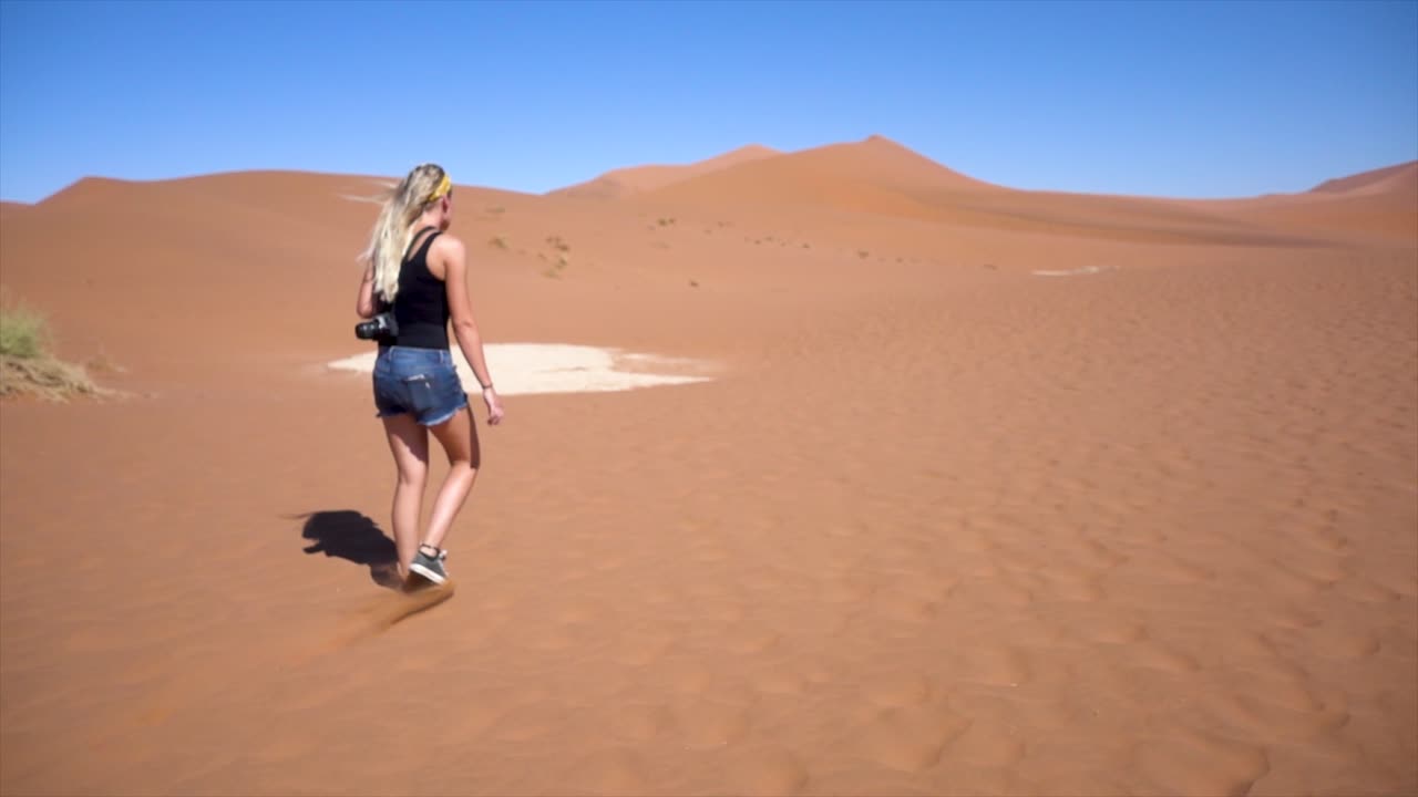 cámara lenta de una joven milenaria caminando en sossusvlei, namibia con una cámara en la espalda