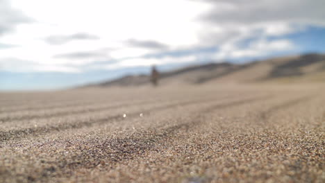 close up of sand blowing with blurred figure walking towards camera in desert