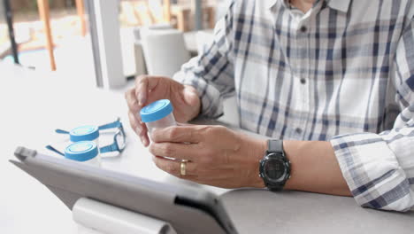 Midsection-of-senior-biracial-man-with-medication-having-tablet-video-call,-slow-motion