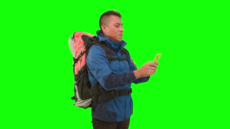 An-adult-Male-holding-a-yellow-smartphone-and-wearing-a-hiking-backpack-in-a-studio-with-green-screen,-texting