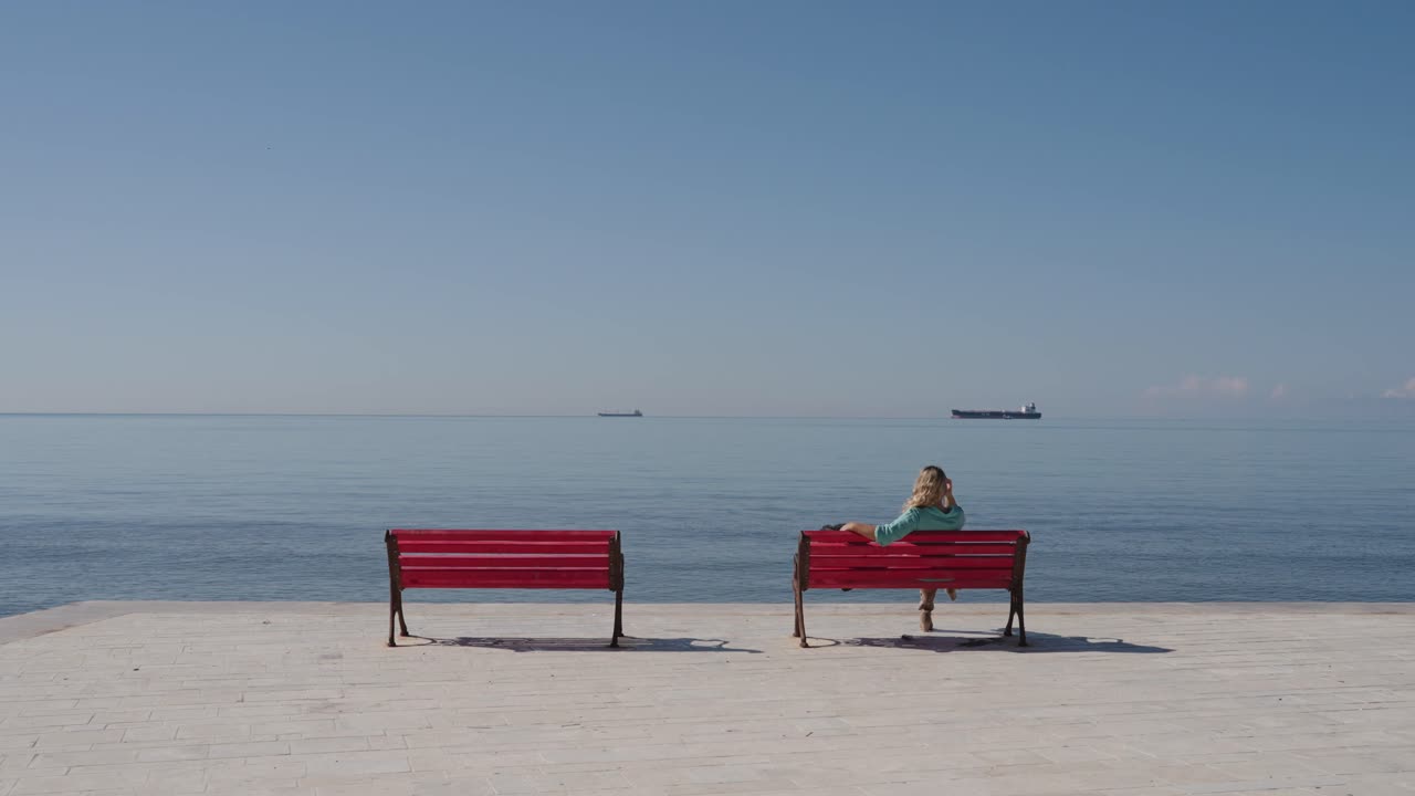 Woman Sits on Red Bench on Boardwalk by the Sea - Static Behind